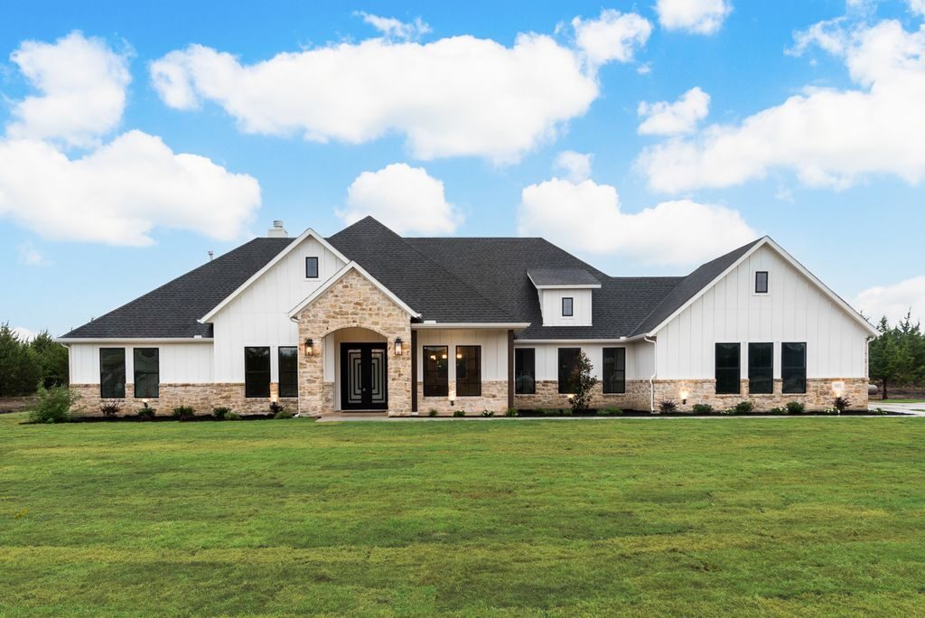 A white board-and-batten custom home with stone accents by LMC Custom Homes, on open Texas acreage